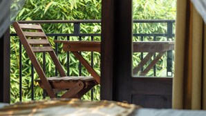 Een kamer met een bed, een houten stoel en een balkon met uitzicht op groen.
