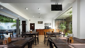 Een restaurant met houten tafels en stoelen, een bar en uitzicht op groen.