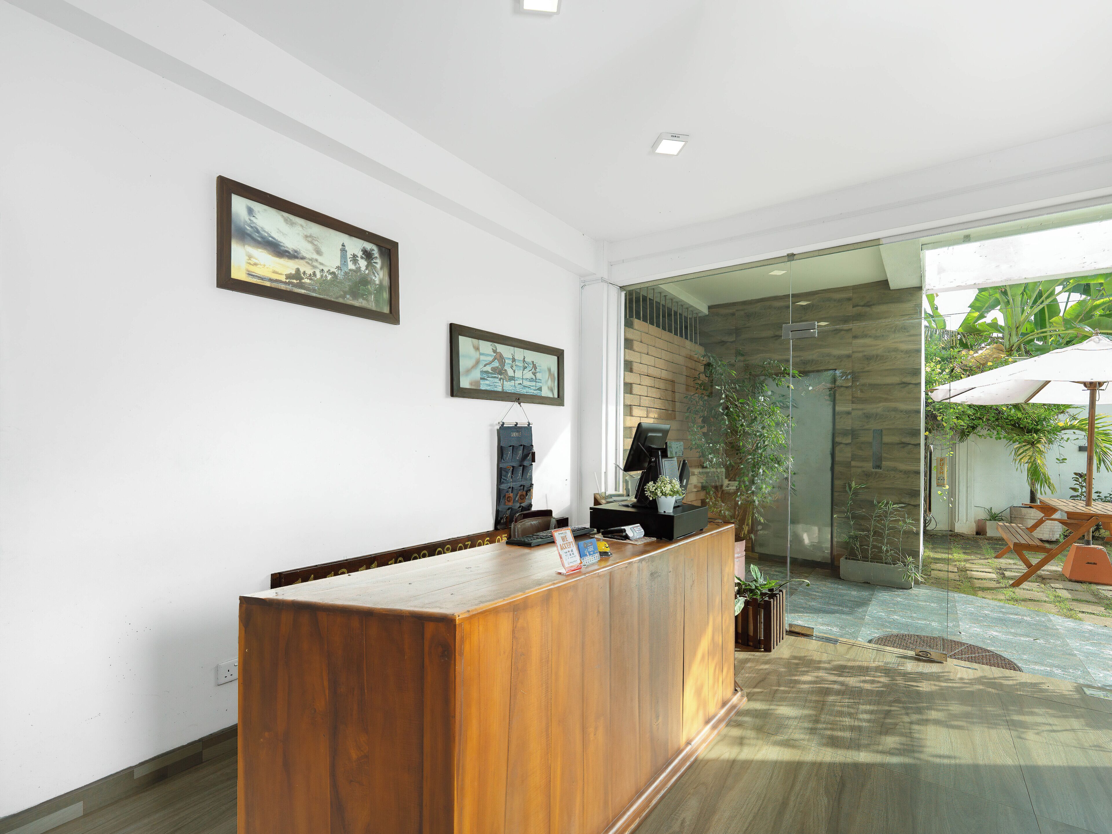 A reception desk with a wooden finish, a glass door leading outside, and two framed pictures on the wall.