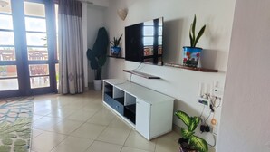 Una sala de estar con un televisor de pantalla plana, un mueble blanco para equipo multimedia y una planta en maceta.