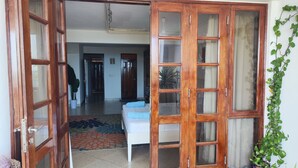 Una habitación con una cama, una puerta de madera, una planta en maceta y suelo de baldosas.