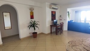 Un salón amplio con suelo de baldosas, una planta en maceta, una zona de comedor con mesa y sillas, y un sofá azul.