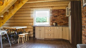 A kitchen with wooden cabinets, a window with a curtain, a table with stools, and a wooden ceiling. - Holiday Homes With Fireplaces, Playground (Lubrza)
