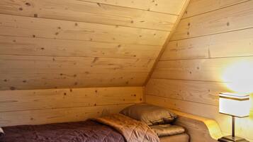 Una habitación pequeña y acogedora con paredes de madera y techo inclinado, con una cama individual con cubrecama acolchado y una lámpara de noche.