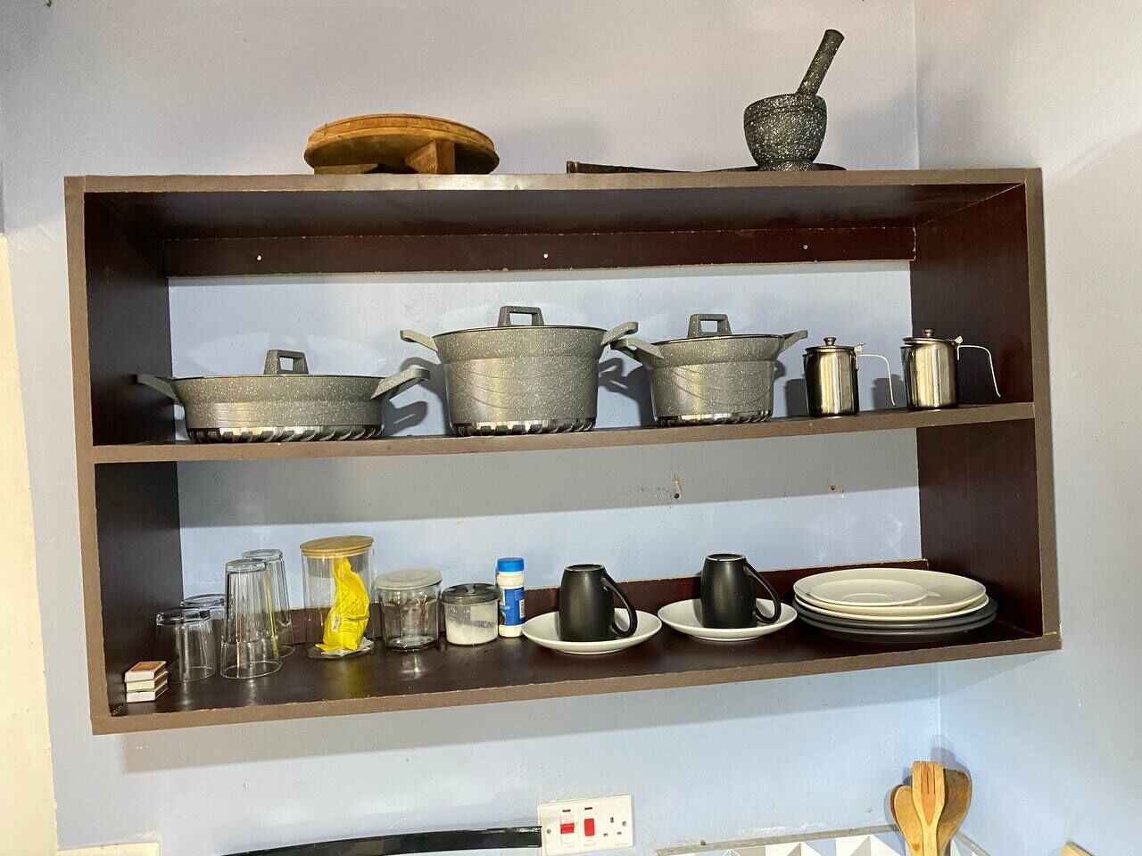 Une étagère de cuisine contenant divers ustensiles de cuisine, de la verrerie et des assiettes.