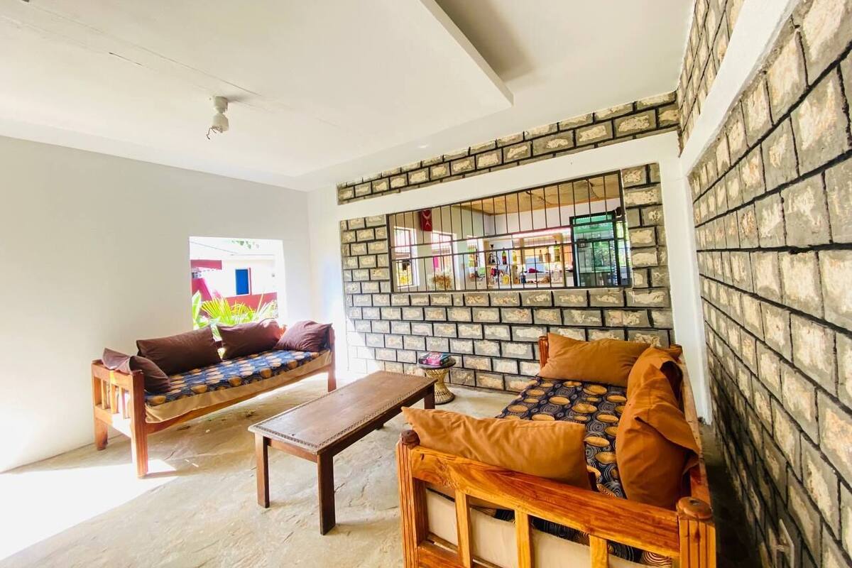 Una habitación con pared de ladrillo, un sofá y una mesa de madera, y una ventana que ofrece vistas a un edificio colorido.