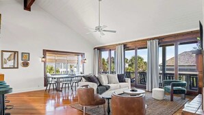 A spacious living room with a high ceiling, a ceiling fan, a dining area with a table and chairs, and large windows with curtains. - Spanish Villa - Sleeps 12 (Jacksonville Beach)