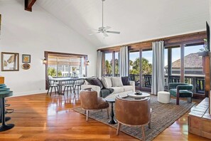 Un vaste salon doté d’un haut plafond, d’un ventilateur de plafond, d’un coin repas avec une table et des chaises, et de grandes fenêtres avec des rideaux.