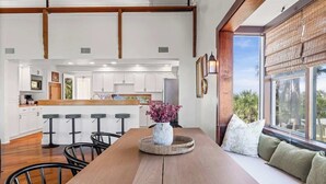 A modern kitchen with white cabinets, a wooden island, and a dining area with a wooden table and bar stools. - Spanish Villa - Sleeps 12 (Jacksonville Beach)