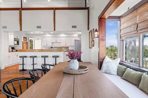 Una cocina moderna con armarios blancos, una isla de madera y un comedor con mesa y taburetes de bar.