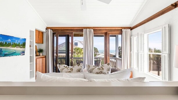A bedroom with a bed, a ceiling fan, large windows, and a view of the sea. - Spanish Villa - Sleeps 12 (Jacksonville Beach)