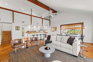 Amplia sala de estar con sofá, sillas, una mesa de centro y una cocina al fondo.