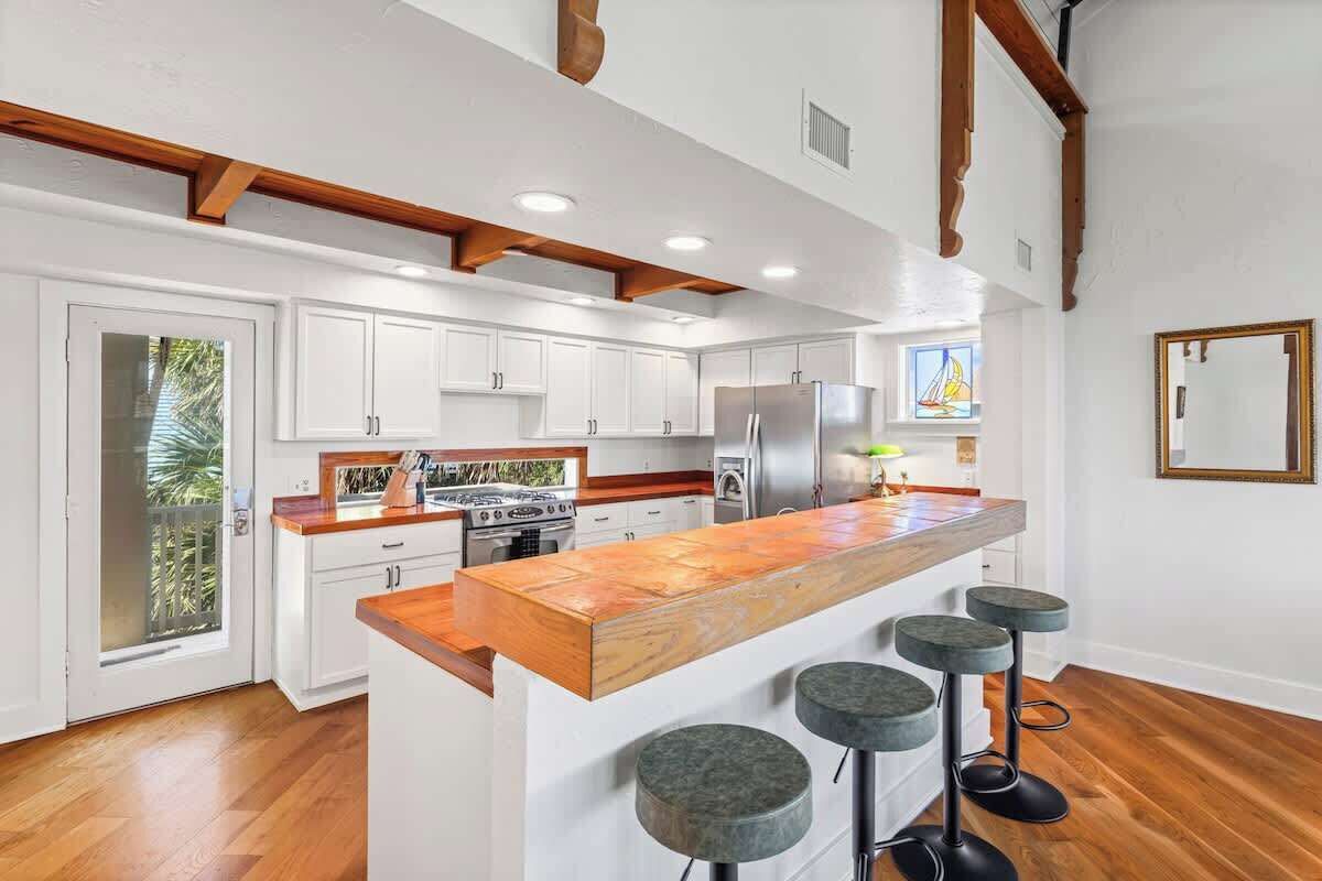 A modern kitchen with white cabinets, a wooden island, and a large refrigerator.