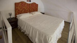 Een eenpersoonsbed met een witte spreidek en een hoofdbord met bloemen in een kamer met houten vloeren en witte muren.