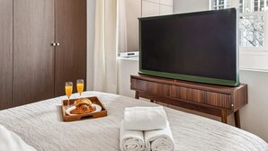 Een hotelkamer met een bed, een televisie, een houten kastje en een dienblad met croissants en sinaasappelsap.