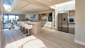 A modern kitchen with a central island, stainless steel appliances, and a large window overlooking a cityscape. - Elegant Coastal Luxury Villa Near Cape Town | Walk to Beach & Dining, sleep 6,  (Cape Town)