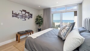 A bedroom with a large bed, a view of the sea, and a plant. - Elegant Coastal Luxury Villa Near Cape Town | Walk to Beach & Dining, sleep 6,  (Cape Town)