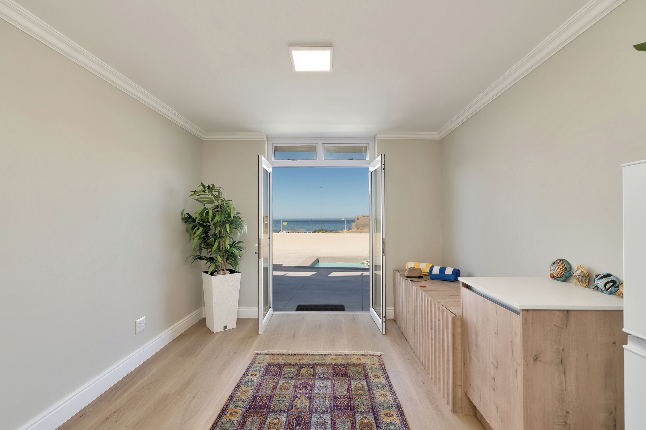 Un pasillo con vista a la playa, una planta en maceta, un armario de madera y una alfombra colorida.