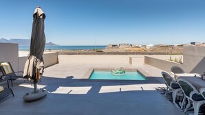 A rooftop pool area with a view of the ocean, a lounge chair, a table, and a covered umbrella. - Elegant Coastal Luxury Villa Near Cape Town | Walk to Beach & Dining, sleep 6,  (Cape Town)