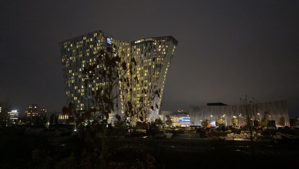 A modern building with a unique angular design, featuring numerous windows and a prominent logo on the facade.