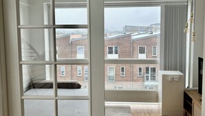 A modern apartment with a large window, a built-in bookshelf, a flat-screen TV, and a wooden floor.