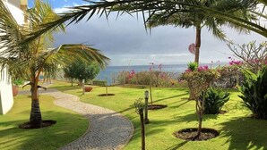 A landscaped garden with a cobblestone pathway, palm trees, and flowering plants. - Superior Rentals - Beachfront Penthouse (free parking) (Funchal)