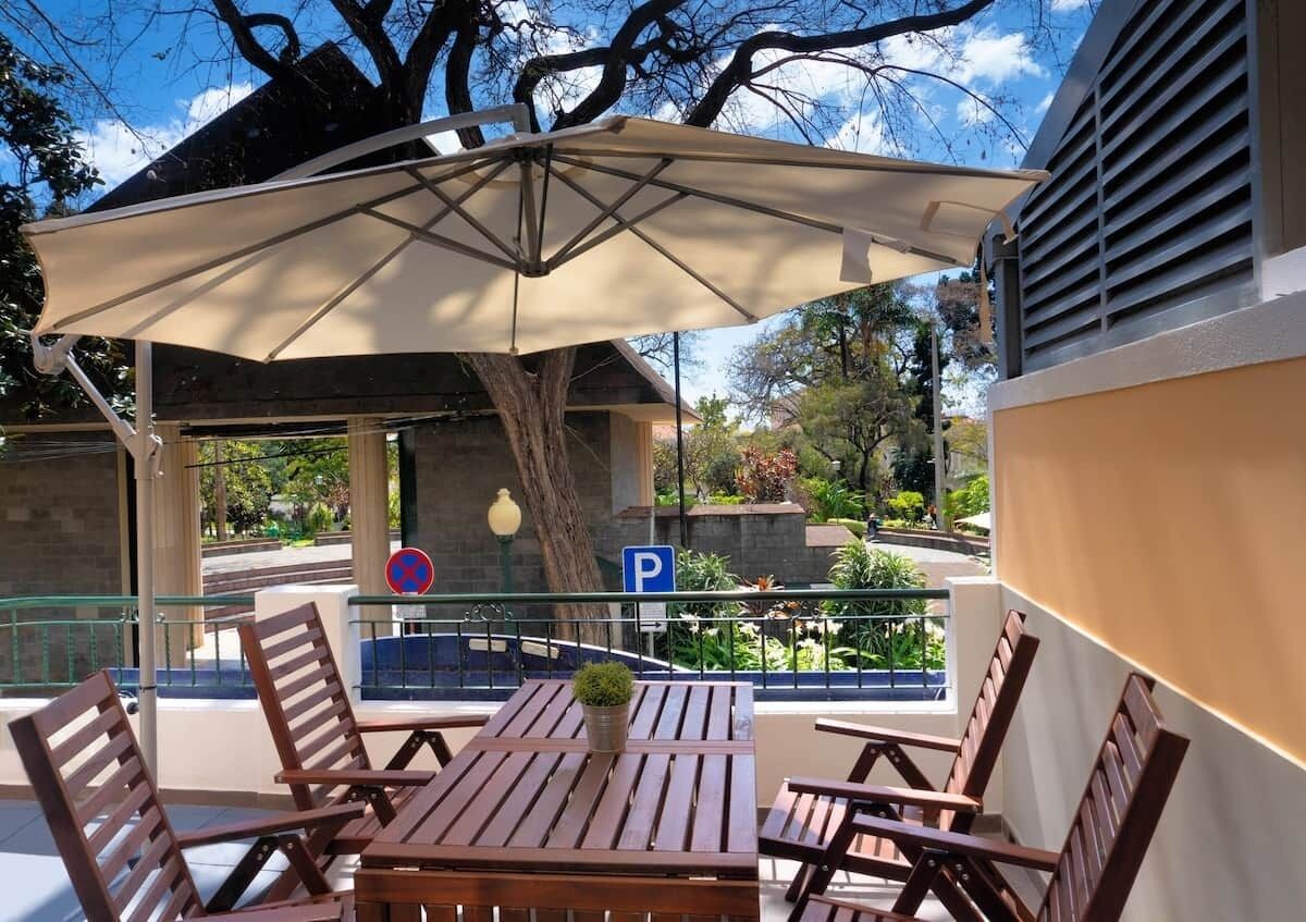 Une terrasse extérieure avec des tables et des chaises en bois, un grand parasol et une vue sur une rue où se trouve un panneau de signalisation indiquant un espace de stationnement.
