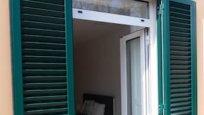 A room with a bed, a nightstand, and a window with green shutters. - Superior Rentals - Downtown Villa (Funchal)