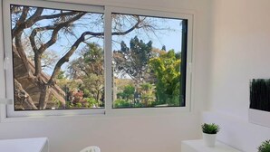 A room with a large window, a white desk, a white chair, and a white cabinet with two potted plants. - Superior Rentals - Downtown Villa (Funchal)