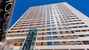 Ein hoch aufragendes Hotel mit modernem Design, das einen markanten Glasaufzug und eine Reihe gleichmäßig angeordneter Fenster zeigt.