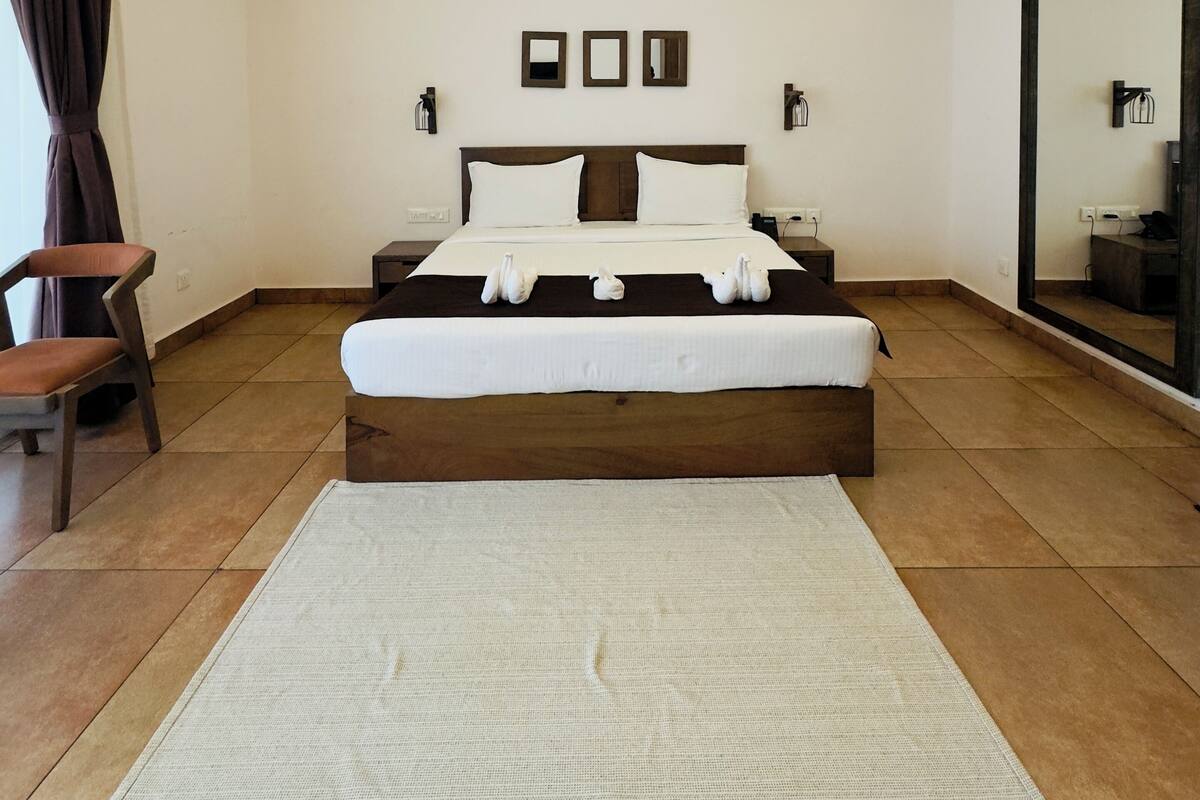 Quarto de hotel moderno com uma cama grande, um espaço para sentar com uma poltrona, um espelho grande e um ventilador de teto.