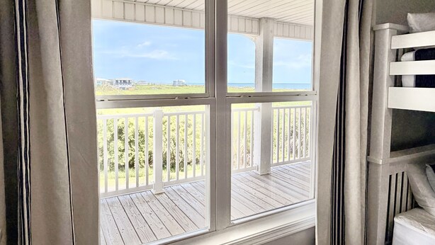 Una habitación con un ventanal grande que da a una terraza de madera y vistas a la playa.