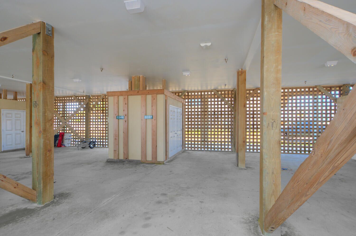 A spacious indoor area with exposed wooden beams, a concrete floor, and a partially constructed wall with a door labeled '3206'.