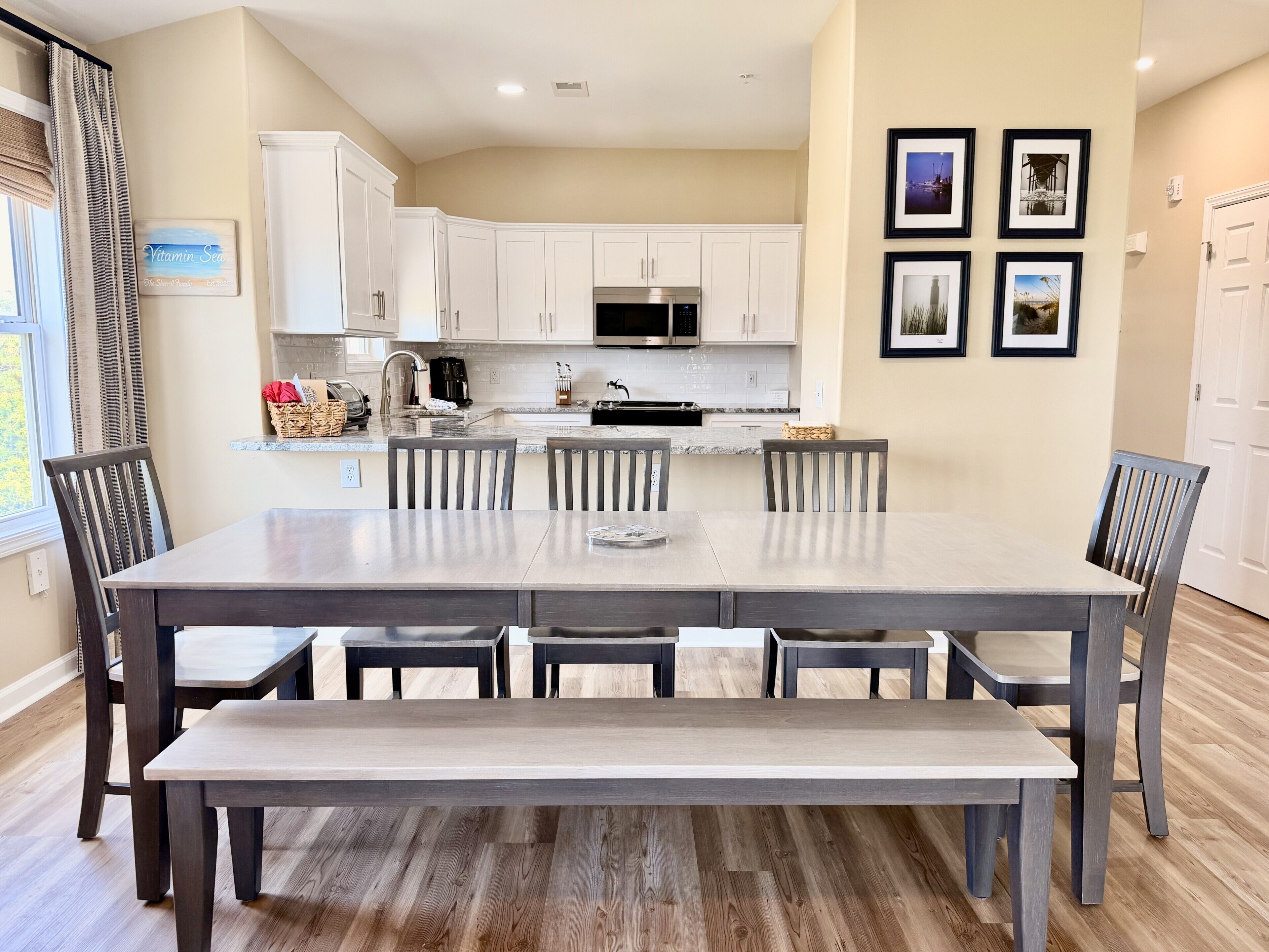 A modern kitchen with white cabinets, a large island, and a dining area with a bench.