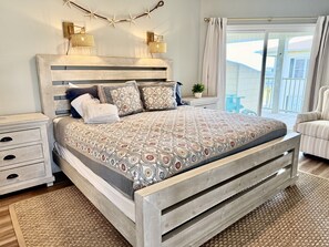 Ein Schlafzimmer mit einem hölzernen Bett, Nachttischen, einer Stehlampe und einem Blick ins Freie.