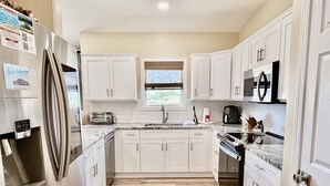 Una cocina con armarios blancos, electrodomésticos de acero inoxidable, un ventanal con vistas y suelo de madera.