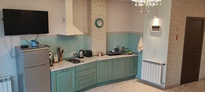 Une cuisine avec des meubles de couleur bleu-vert, un réfrigérateur en acier inoxydable, un téléviseur à écran plat, une bouilloire, un grille-pain et une horloge murale.