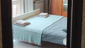 Un dormitori amb un llit, un radiador, un armari de fusta i una finestra amb cortines.