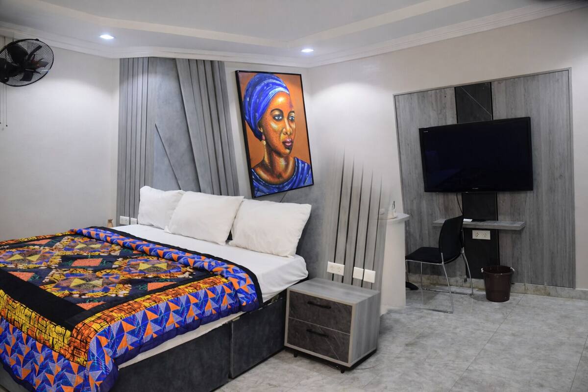 A modern bedroom with a large bed, a TV, and a painting on the wall.