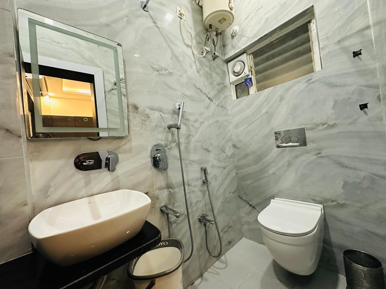 A bathroom with a marble wall, a sink, a toilet, and a shower.
