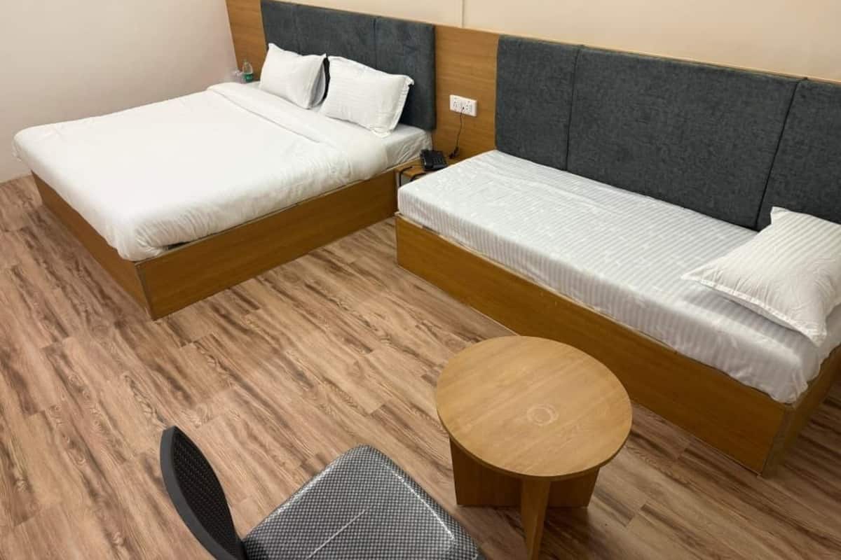 Quarto com duas camas, uma mesa redonda de madeira e uma cadeira.