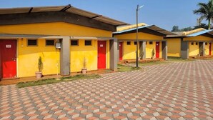 A row of yellow buildings with red doors, each with a small potted plant in front. - Saputara valley View (Ahwa)