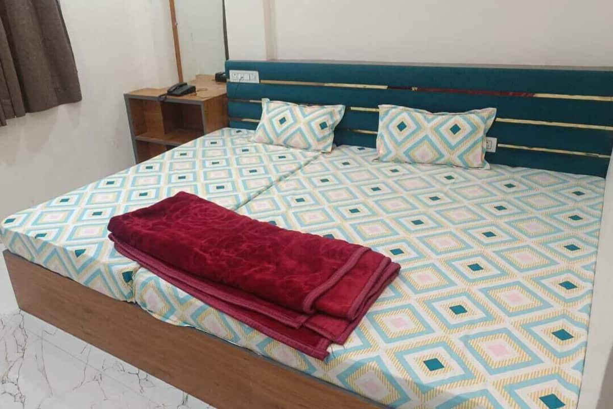 A bed with a geometric patterned bedspread and pillows, a wooden headboard, a bedside table with a phone, and a window with curtains.