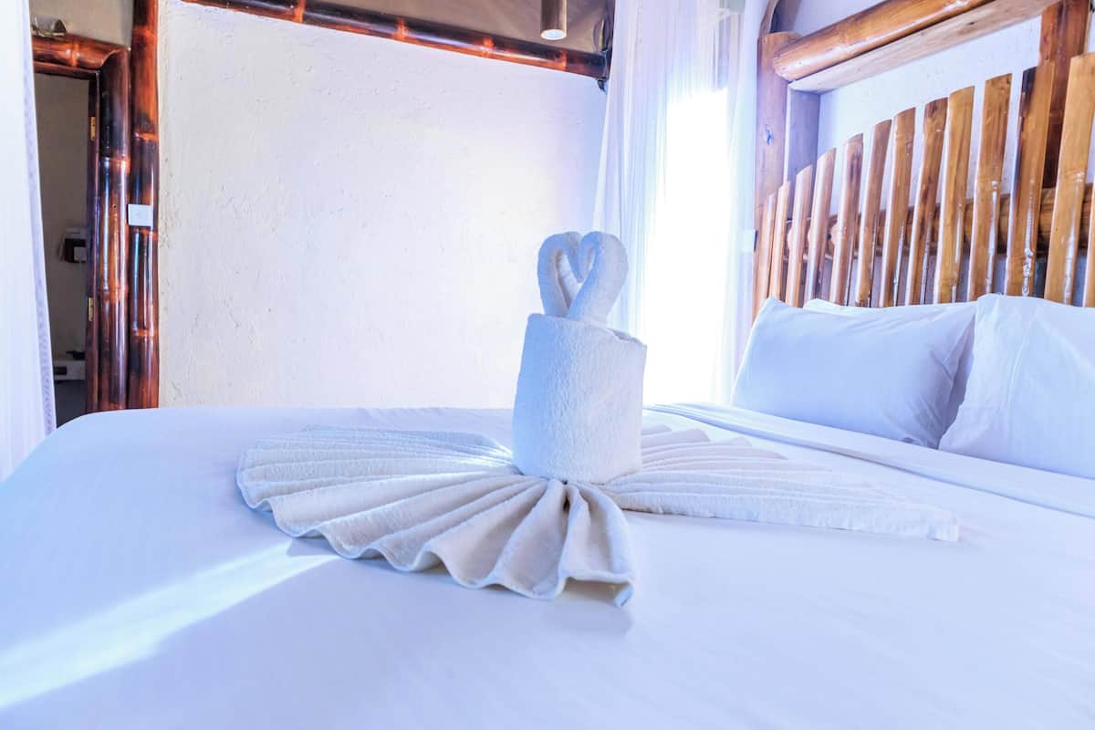 Un lit bien fait, avec une serviette disposée en forme de cœur, une tête de lit en bois et un mur blanc.