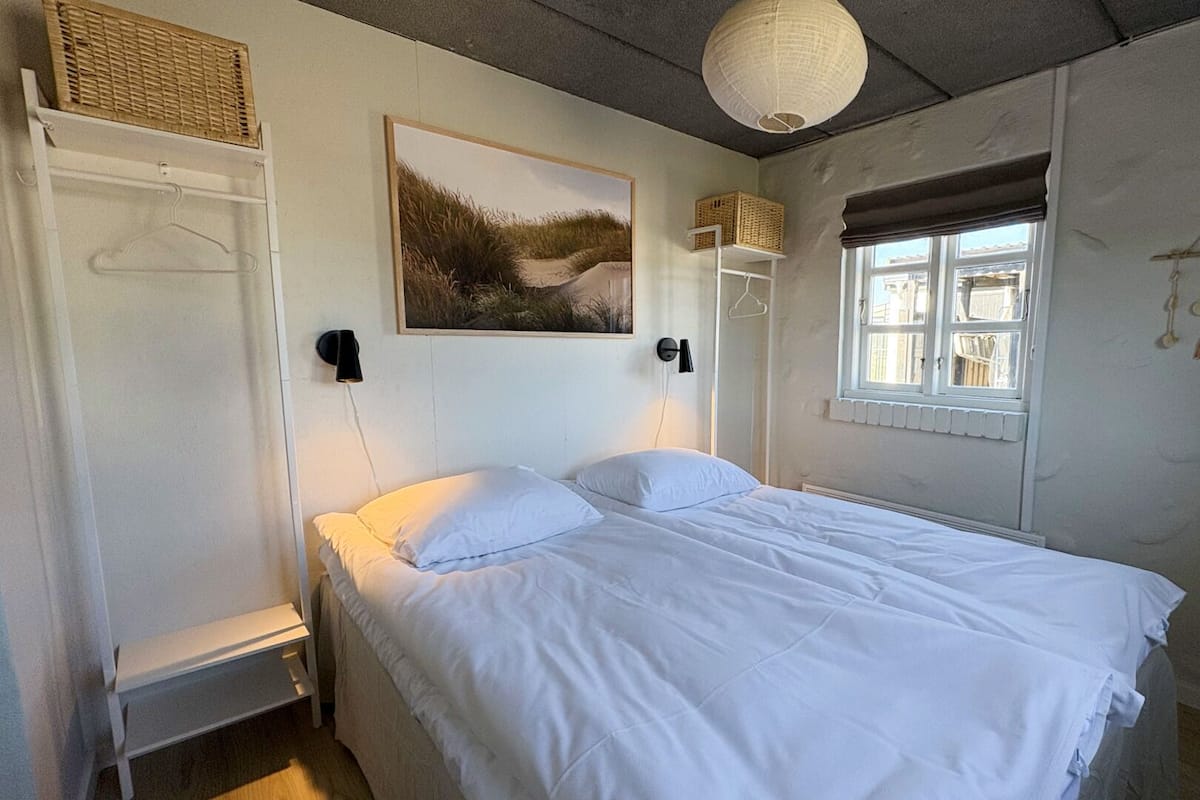 Une chambre à coucher avec un lit, une fenêtre, une lampe fixée au mur et un tableau.