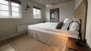 A bedroom with a bed, a bedside table, a lamp, a window, and a wall-mounted picture.