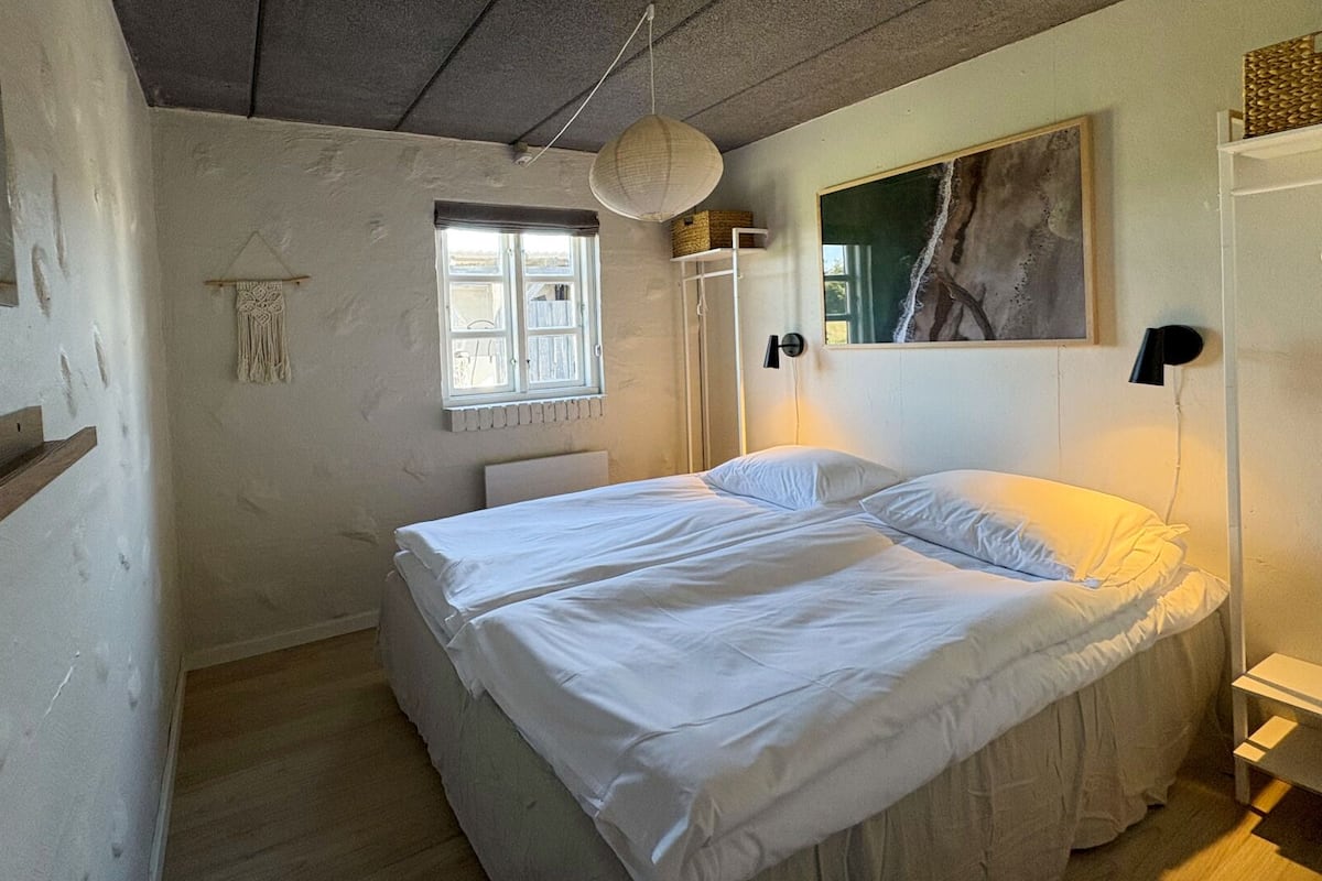 Une chambre à coucher avec un lit, une fenêtre, un luminaire suspendu et un tableau au mur.