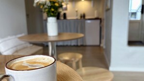 A cup of coffee on a wooden table in a modern kitchen with a dining area in the background.