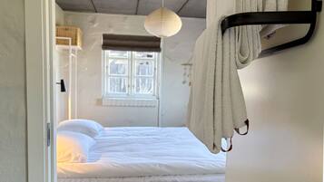 Un dormitorio con cama, lámpara colgante, ventana con persianas y un toallero.
