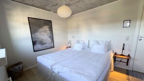 Un dormitorio con una cama grande, un aplique de pared, un cuadro enmarcado y una mesita de noche pequeña.